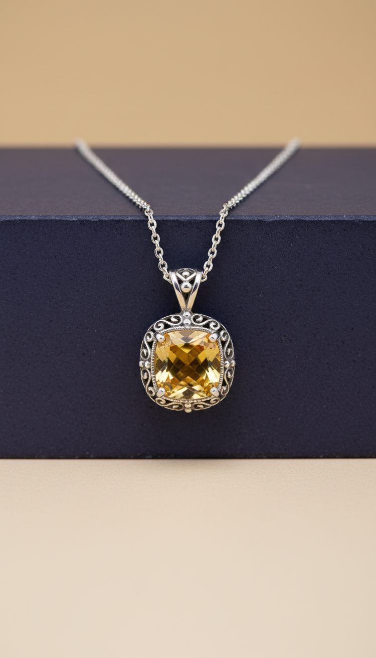 Yellow sapphire pendant with an ornate silver border and silver chain on a navy display