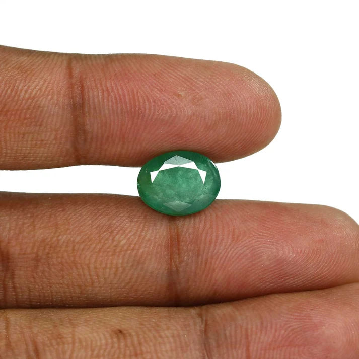 Natural green oval faceted emerald Panna gemstone held between fingers for scale and clarity by Bright Blue Gemstones in Bellandur, Bengaluru