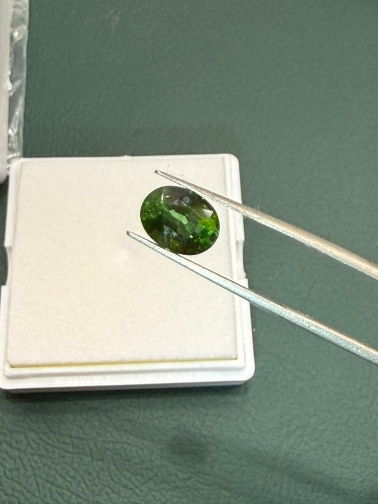 Gemologist inspecting a natural green oval sapphire gemstone using precision tweezers over a gemstone display box at Bright Blue Gemstones store in Bellandur, Bengaluru