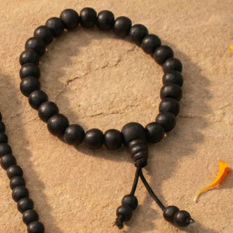 Black beaded mala necklace with tassel on a textured surface with flowers.